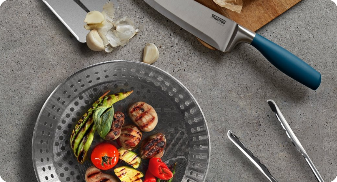 Plan de travail de cuisine avec couteau, pince et assiette de légumes grillés.