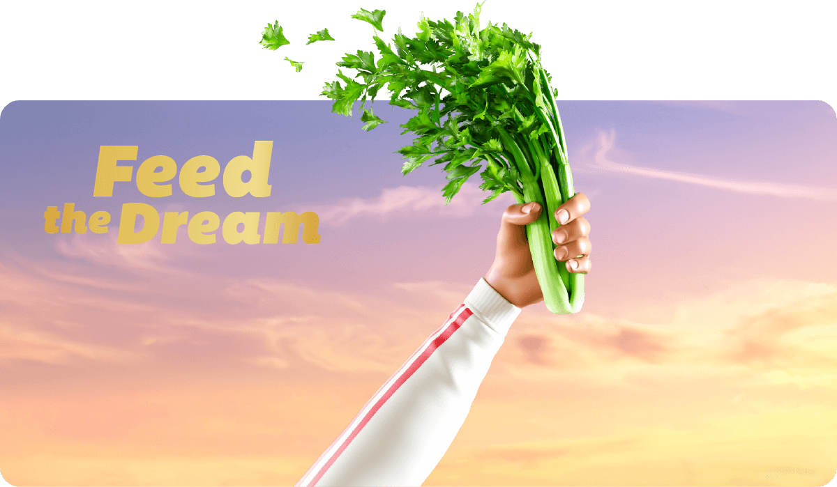 Athlete's arm and hand, wearing a white sleeve with a red stripe, holding a bunch of celery, raised against a sunset sky to mimic the Olympic flame.